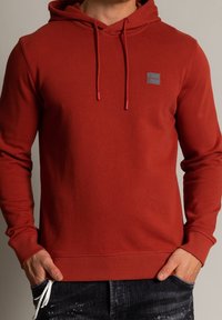 Röd hoodie i bomullsblandning, med en framtill placerad ficka, justerbar dragsko runt huvan och tonad logotypapplikation på bröstet.