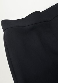 Pantalon noir en tissu lisse, avec une taille épurée et une coupe ajustée. Design simple, sans matériel ou motifs visibles.