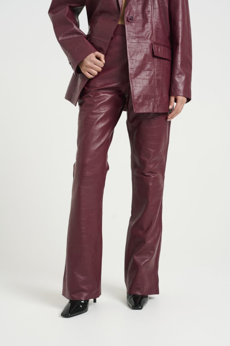 Burgundy faux leather suit featuring a structured blazer and flared pants with a crocodile texture. Glossy black pointed-toe heels.