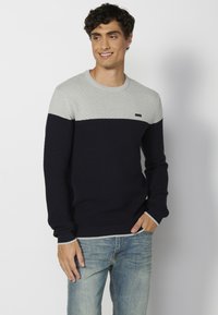 Adīts džemperis gaiši pelēkā un tumši zilā krāsā, ar teksturētu rakstu, apaļu kakla izgriezumu un ribotām aproču un apakšmalas malām. Redzama neliela ar zīmolu apzīmēta birka.