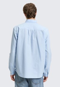 Ανοιχτό μπλε πουκάμισο με μακριά μανίκια από λείο ύφασμα. Διαθέτει κλασικό γιακά και πατιλέτα με κουμπιά και μανσέτες με κουμπιά.