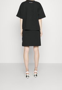 Černé oversized tričko s kulatým výstřihem a krátkými rukávy, kombinované s přiléhající černou sukní. Nosit ve společnosti bílých otevřených lodiček.