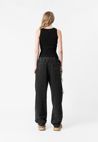 Top negro de tirantes combinado con pantalones negros holgados que cuentan con bolsillos laterales, cinturilla elástica y un detalle de cordón. Textura suave.