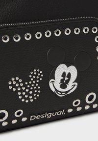 Borsa in pelle nera strutturata con un design argentato di Topolino, borchie decorative argentate e logo "Desigual". Chiusura superiore con zip.