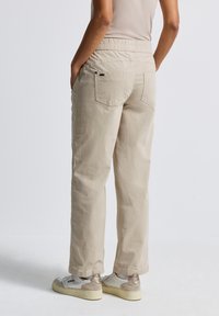 Pantalons en coton beige avec une coupe décontractée, taille élastique et poches arrière. Portés avec des baskets blanches et beiges. Tissu texturé.
