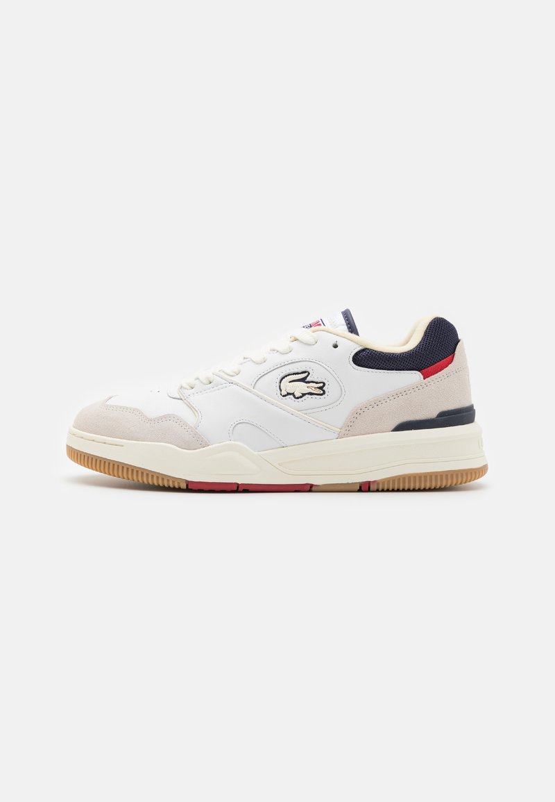 Zapatillas deportivas blancas con una mezcla de materiales de cuero liso y ante, acentos en azul marino y suela de goma. Logotipo de Lacoste en el lateral.