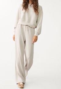 Lys beige sweat-sweater og matchende bukser i blødt stof, der har en afslappet pasform, ribbede manchetter og en justerbar snoretræk i taljen.