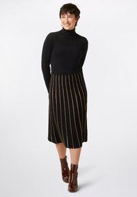 Black knit turtleneck with textured detail, paired with a black skirt featuring gold vertical stripes. Worn with brown ankle boots.