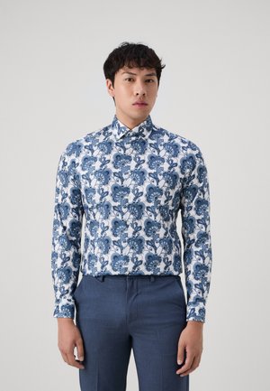 Skjorta med långa ärmar i blått blommönster på vit bakgrund, med knäppning vid kragen och en kroppsnära passform, matchad med marinblå dressbyxor.