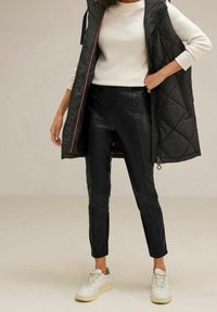 Černý prošívaný vest s krémovým dlouhým rukávem, kombinovaný s černými kalhotami z umělé kůže a bílými teniskami. Jednoduchý, elegantní a moderní design.