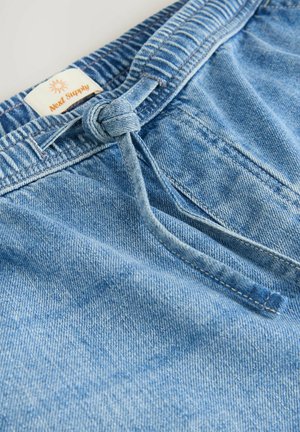 Ljusblå denimshorts med elastisk midja och dragsko. Har en liten etikett med "Next Supply"-logotyp. Slät textur.