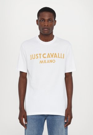 T-shirt en coton blanc à manches courtes avec un texte jaune audacieux "JUST CAVALLI MILANO" sur le devant. Coupe simple et décontractée.