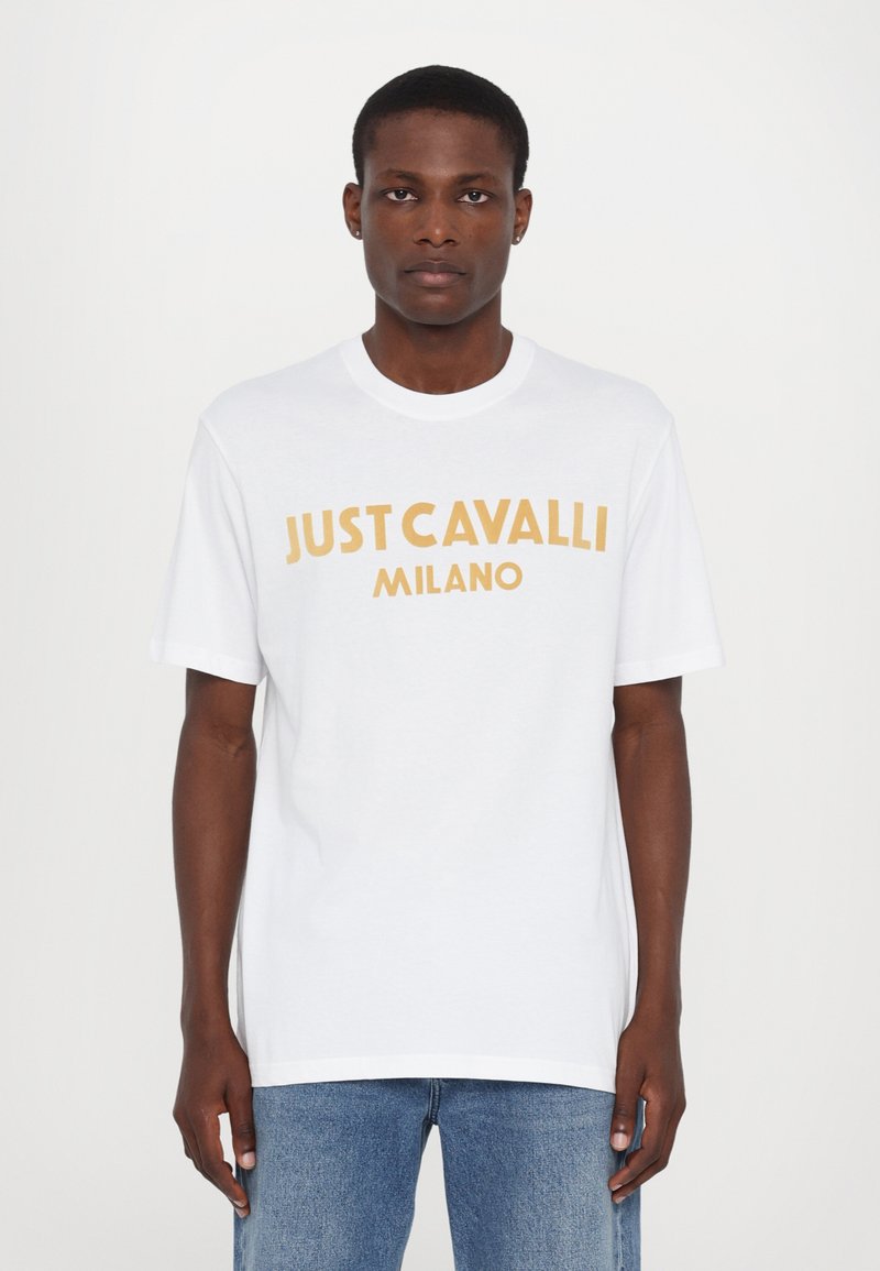 Bílá bavlněná tričko s krátkými rukávy, na přední straně s výrazným žlutým nápisem "JUST CAVALLI MILANO". Jednoduchý, volný střih.
