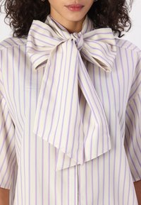 Bluză bej cu dungi verticale subțiri în lavandă și violet. Are un guler mare în stil funda și mâneci scurte. Material neted, ușor.