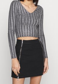 Mujer con un top de rayas gris de manga larga y un mini falda negra con dos cremalleras plateadas verticales en la parte delantera.