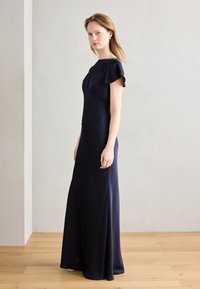 Rochie lungă până la podea, de culoare bleumarin, cu mâneci scurte în formă de flutur și un corset ajustat. Țesătură netedă cu detalii subtile de drapare.