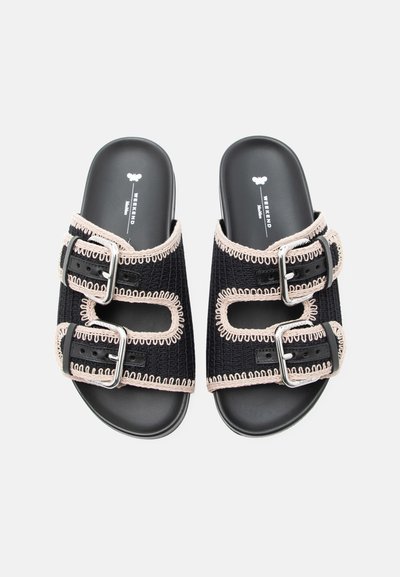 Μαύρα σανδάλια με δύο ρυθμιζόμενες ασημένιες αγκράφες και μπεζ διακοσμητικό ράψιμο σε υφασμάτινους ιμάντες πάνω από επίπεδες σόλες.