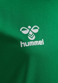 Grøn t-shirt med tekstureret stof, der har et hvidt logo af en stiliseret bi og ordet "hummel" i fed skrift nedenfor.