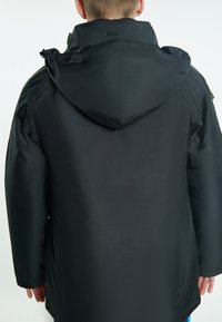 Svart vattentät jacka med huva, med en slät yta, långa ärmar och en något lös passform. Inga synliga mönster eller detaljer.