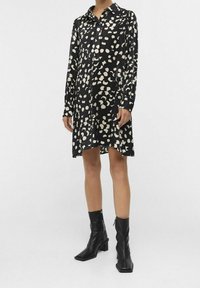 Robe noire à manches longues, col à revers et motif abstrait crème. Associée à des bottines en cuir noires avec des bouts carrés.