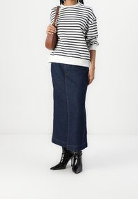 Sudadera a rayas blancas y negras con cuello redondo, combinada con una falda larga de mezclilla oscura y botas negras de tacón alto con punta afilada.