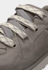 Baskets en daim gris clair avec des panneaux en maille texturée, des lacets contrastants crème et gris à motif diamant, et une semelle blanche épaisse.