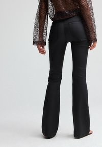 Black flared jeans with a smooth texture, featuring back pockets and a mid-rise waist, paired with a sheer sequined top.
