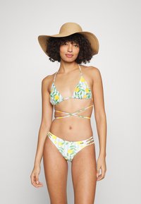 Conjunto de biquíni com um padrão de limões e folhas sobre um fundo branco. Top triangular com alças ajustáveis e recortes laterais na parte inferior.