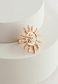 Rosaguld ring med et soldesign, der har teksturerede stråler og en cirkulær center. Selve ringen er enkel og glat, hvilket komplementerer den intrikate top.