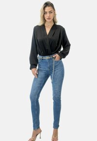 Svart satin långärmad omslagblus i kombination med hög midja blå skinny jeans, accentuerad av ett kedjebälte och klara högklackade sandaler.