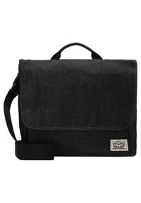 Bolsa mensajera de mezclilla negra con cierre de solapa, asa superior y correa ajustable. Presenta una etiqueta con el logo tejido en el frente.