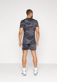 Črno-siva tie-dye športna oblačila, ki vključujejo majico s kratkimi rokavi in kratke hlače, izdelana iz elastičnega blaga s prilegajočo se zasnovo.