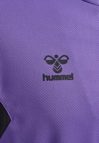 Lila Sportshirt aus strukturiertem Material, mit einem schwarzen Hummel-Logo und einem kontrastierenden schwarzen Designelement an der Seite.