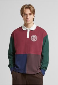 Langærmet polo-skjorte med farveblokdesign i burgunderrød, grøn, marineblå og brun. Hvid krave med broderet logo-detalje.