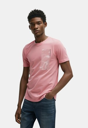 T-shirt sportivo rosa chiaro, maniche corte, collo rotondo, con una stampa grafica testurizzata sul lato sinistro del petto e dettagli di branding discreti.