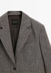 Blazer grigio con texture, colletto a pistola, chiusura a un bottone e taschino sul petto, etichettato "Massimo Dutti" e realizzato in Portogallo.