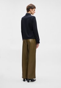 Črn dolg rokav top z sproščenim krojem, kombiniran z olivno zelenimi visokim pasom širokimi hlačami in črnimi škornji s peto.