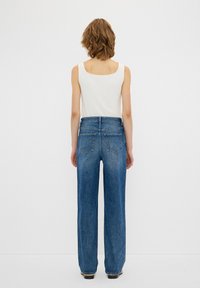 Jeans a gamba larga blu con vita alta, tasche posteriori e una consistenza liscia, abbinati a un top bianco senza maniche.