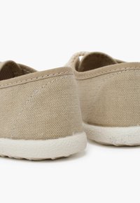 Scarpe in tela beige con una tomaia in tessuto testurizzato e suole in gomma bianche, caratterizzate da cuciture a vista e un design semplice e arrotondato.