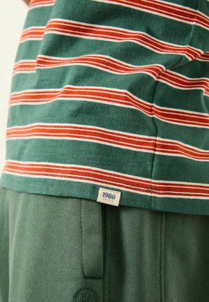 Zelené pruhované tričko s červenými a bílými vodorovnými pruhy, s visačkou "1988" a doplněné o zelené kalhoty, prezentující texturovanou tkaninu.