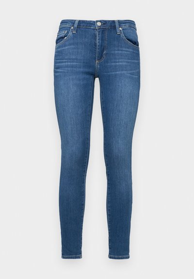 Skinny blue jeans in denim material, featuring a mid-rise waist, five-pocket design, and a smooth texture with minimal fading.