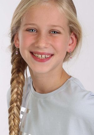 Zilveren oorbellen met een roze cupcake ontwerp op een meisje met lang gevlochten blond haar, dat een lichtblauwe t-shirt draagt en glimlacht.