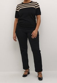 Musta lyhythihainen paita, jossa on vaaleanruskeat raidat rinnalla, yhdistetty mustiin suoralahkeisiin farkkuihin ja mustiin Mary Jane -korkokenkiin. Pehmeä, joustava kangas.