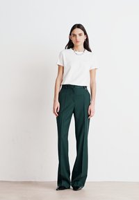 Pantalones verdes ajustados con cintura alta, frente plisado y un acabado suave, combinados con una camiseta blanca de cuello redondo.
