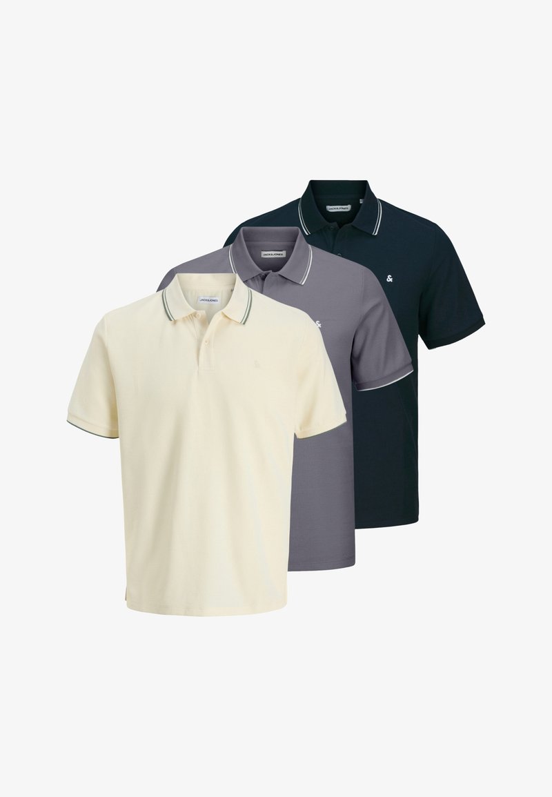 Drei Poloshirts ausgestellt: blassgelb, grau und marineblau, jeweils mit einem kontrastierenden Besatz am Kragen und an den Ärmeln, mit einem kleinen Logo.