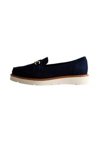 Chaussure navy en suède à enfiler avec un bout rond, semelle intermédiaire beige et un accent doré à l'avant. Présente une surface texturée et des coutures discrètes.