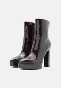 Γυαλιστερά καφέ μποτάκια με τακούνι στον αστράγαλο, με μυτερή μύτη, πλατφόρμα και λεπτομέρεια φερμουάρ στο πλάι. Λείος πατίνα και κομψός σχεδιασμός.