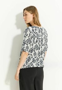 Top con estampado floral en gris claro con diseños en azul marino oscuro. Mangas cortas y un corte relajado, combinado con pantalones negros. Textura de tela suave.
