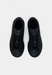 Pár černých tenisek Adidas Stan Smith, zobrazený zvrchu na jednoduchém bílém pozadí s zavázanými tkaničkami.