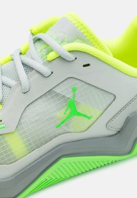 Grå atletisk sko med neongröna accenter, mesh-övre och rutmönster. Har en texturerad sula för grepp och en jumpman-logotyp.